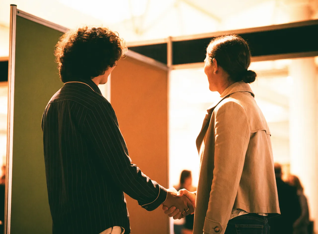 Two people shaking hands beside an exhibition booth, mid-conversation
